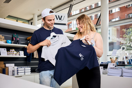 Ein Mann und eine Frau vergleichen T-Shirts im WU Shop.