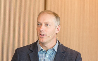 Portrait von Matt Chadder, ein Mann im Anzug und mit Vortragsmikrofon um seinen Kopf, während er spricht