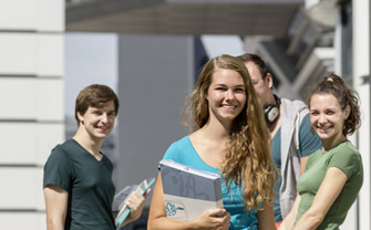 Studierende stehen vor dem LC und blicken lächelnd einer Kollegin mit einer Mappe in der Hand nach.